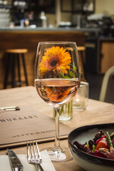 酒杯上的白葡萄酒，餐桌上橙色非洲菊菊花旁的灰色不锈钢刀叉旁